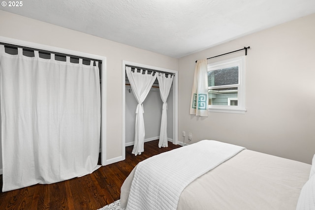 bedroom with baseboards, a textured ceiling, wood finished floors, and multiple closets