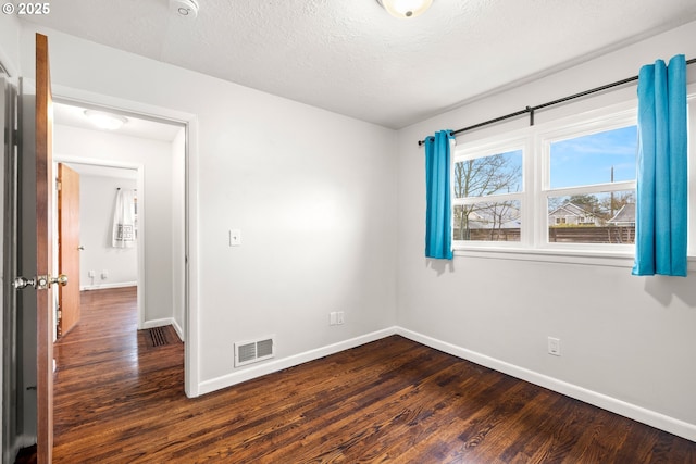 unfurnished room with dark wood finished floors, baseboards, visible vents, and a textured ceiling