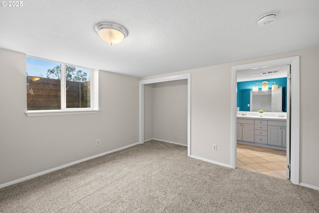 unfurnished bedroom featuring baseboards, light carpet, a textured ceiling, and ensuite bath