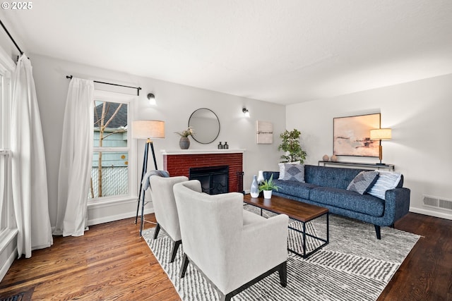 living room with visible vents, a brick fireplace, baseboards, and wood finished floors