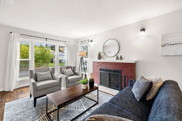 living room with a brick fireplace, a textured ceiling, baseboards, and wood finished floors