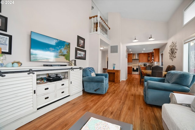 living area featuring a high ceiling, light wood-style floors, and visible vents