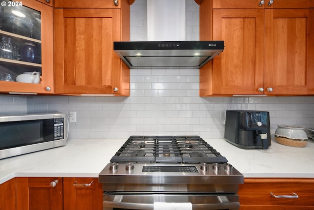 kitchen with decorative backsplash, wall chimney exhaust hood, brown cabinetry, and stainless steel appliances