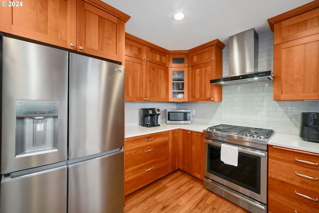 kitchen with light countertops, wall chimney range hood, light wood finished floors, and stainless steel appliances