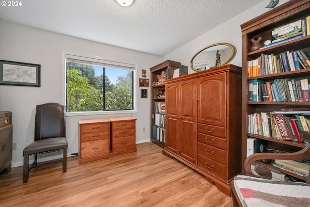 living area featuring light wood-type flooring, baseboards, and a textured ceiling