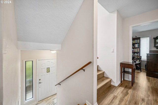 foyer featuring light wood-style flooring, a textured ceiling, baseboards, and vaulted ceiling