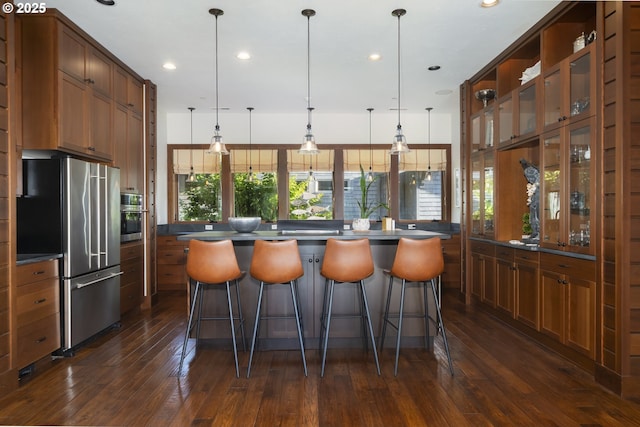 7850 Brooten Mountain Loop, Pacific City, OR 97135 - kitchen featuring appliances with stainless steel finishes, dark countertops, dark wood finished floors, brown cabinets, and a kitchen bar