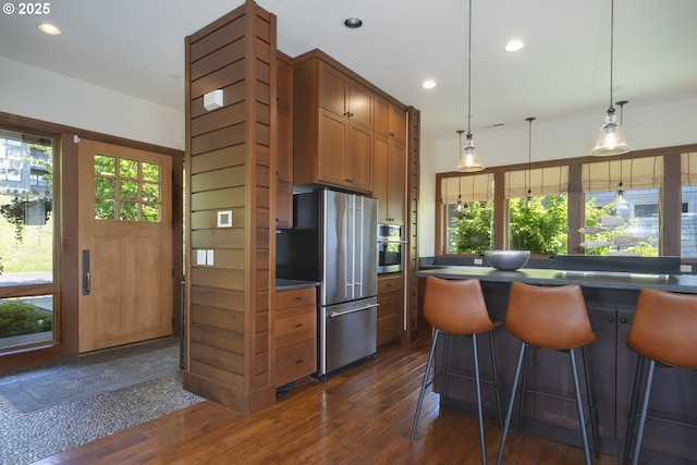 7850 Brooten Mountain Loop, Pacific City, OR 97135 - kitchen with appliances with stainless steel finishes, dark countertops, dark wood-style flooring, brown cabinets, and a breakfast bar