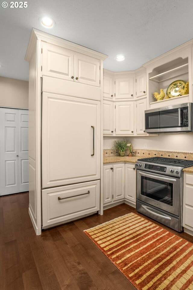 kitchen featuring light stone countertops, appliances with stainless steel finishes, open shelves, a sink, and dark wood finished floors