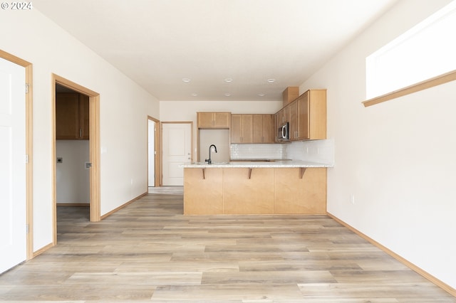 kitchen with kitchen peninsula, a kitchen breakfast bar, backsplash, sink, and light hardwood / wood-style flooring