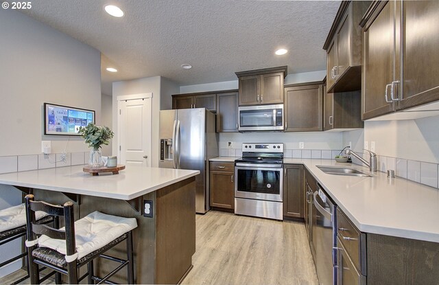 7407 NE 136th Ave, Vancouver, WA 98682 - kitchen with stainless steel appliances, light wood-style flooring, dark brown cabinetry, a kitchen bar, and light countertops