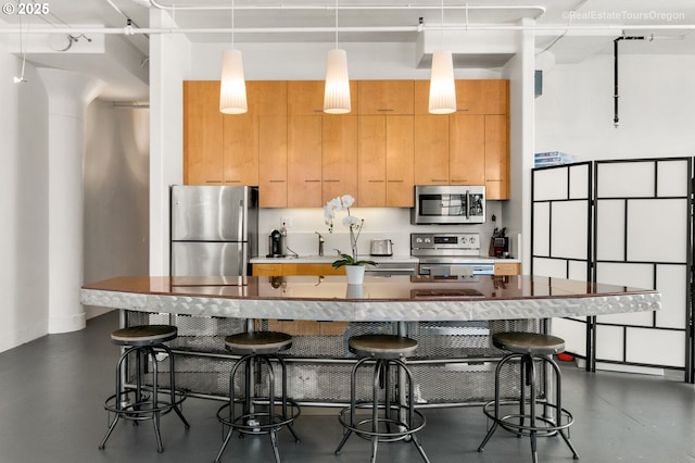 1314 NW Irving St Unit 510, Portland, OR 97209 - kitchen featuring appliances with stainless steel finishes, an island with sink, a breakfast bar area, pendant lighting, and concrete floors