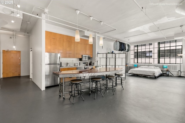 1314 NW Irving St Unit 510, Portland, OR 97209 - kitchen with stainless steel appliances, concrete flooring, a center island with sink, a breakfast bar area, and a high ceiling
