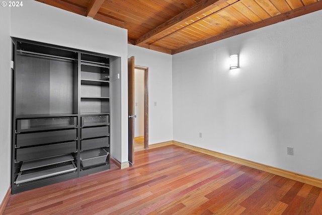 unfurnished bedroom featuring baseboards, wooden ceiling, beamed ceiling, wood finished floors, and a closet