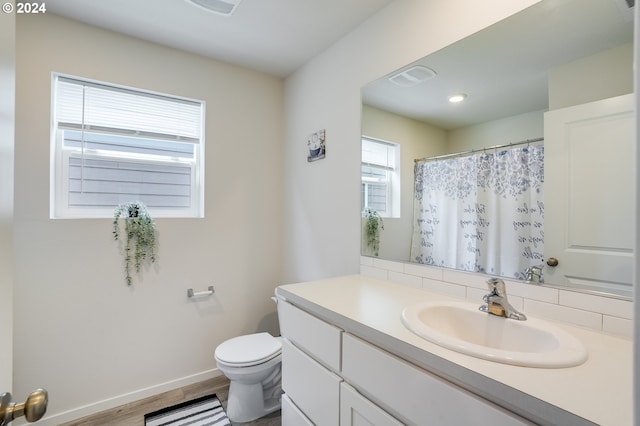 bathroom with vanity, visible vents, toilet, wood finished floors, and baseboards