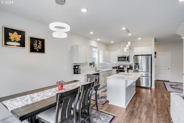 kitchen featuring a sink, light countertops, appliances with stainless steel finishes, white cabinetry, and wood finished floors