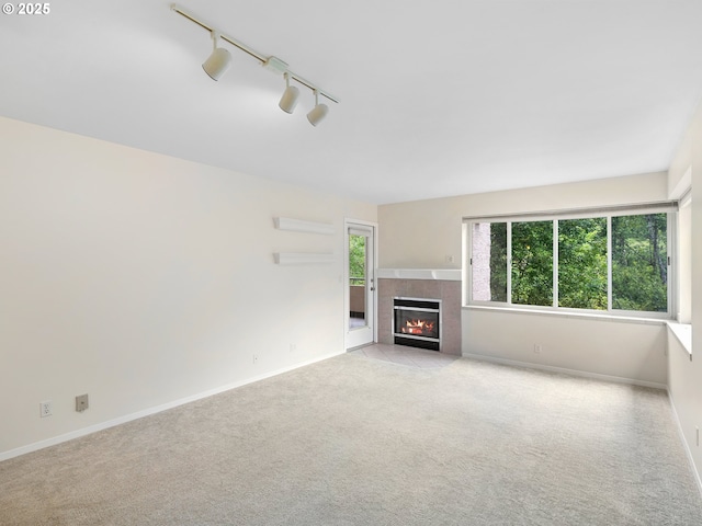 unfurnished living room featuring a fireplace, light colored carpet, and rail lighting