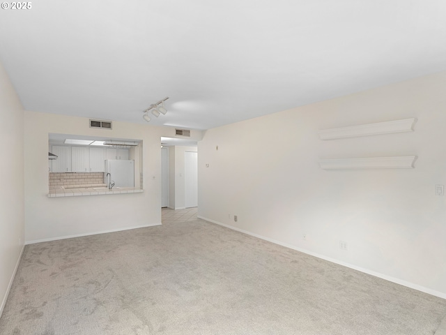 unfurnished living room with rail lighting, sink, and light colored carpet