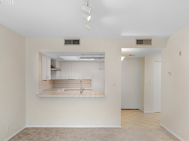 kitchen with light carpet, kitchen peninsula, white fridge, decorative backsplash, and white cabinets