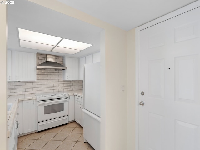 kitchen featuring light tile patterned flooring, tasteful backsplash, white cabinets, white appliances, and wall chimney exhaust hood