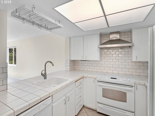 kitchen with tile countertops, sink, white cabinets, wall chimney range hood, and white appliances