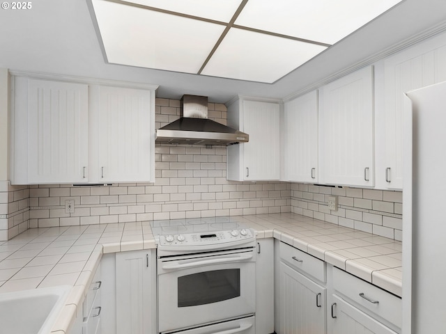 kitchen featuring white cabinetry, tile counters, white range with electric cooktop, decorative backsplash, and wall chimney range hood