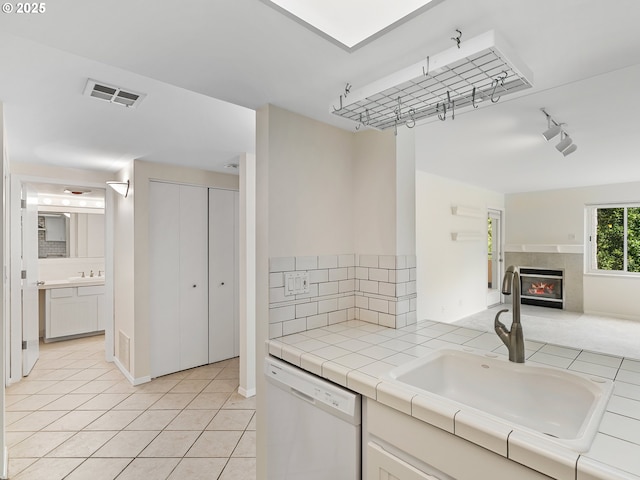 kitchen with a tile fireplace, sink, tile counters, light tile patterned floors, and white dishwasher