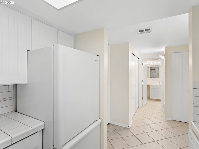 kitchen with white refrigerator, white cabinetry, tile countertops, and light tile patterned floors