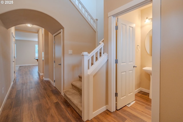 stairs with wood finished floors, arched walkways, and baseboards