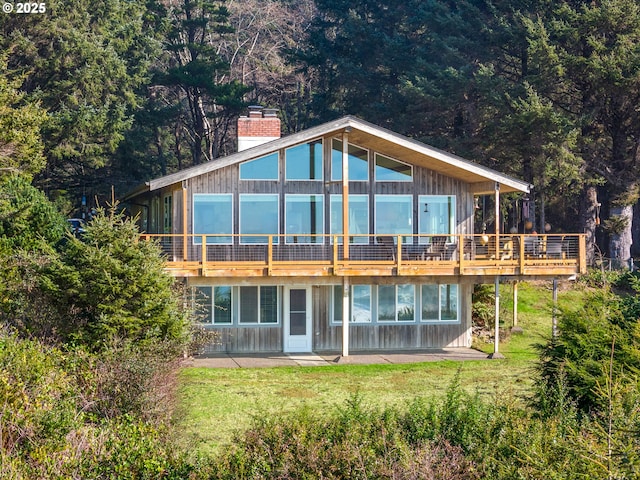 rear view of property featuring a view of trees, a wooden deck, a lawn, and a chimney