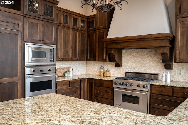 3232 NW Spencer St, Portland, OR 97229 - kitchen with stainless steel appliances, a chandelier, dark brown cabinetry, glass insert cabinets, and decorative backsplash