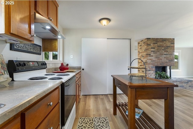 kitchen with electric range, brown cabinets, under cabinet range hood, light wood finished floors, and a fireplace