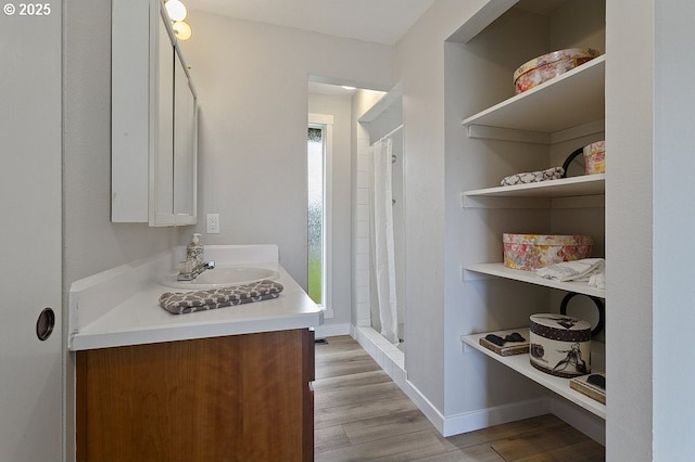 full bathroom featuring wood finished floors, a shower stall, vanity, and baseboards