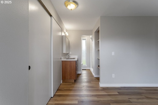 corridor with built in features, wood finished floors, baseboards, and a sink