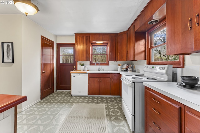 kitchen with white appliances, light floors, baseboards, a sink, and light countertops