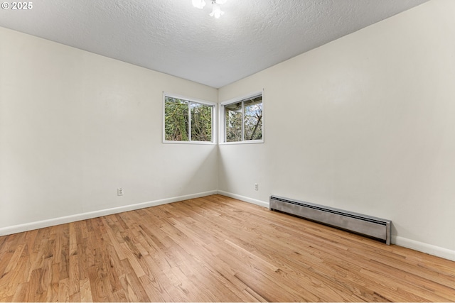 spare room with a textured ceiling, a baseboard heating unit, baseboards, and wood finished floors