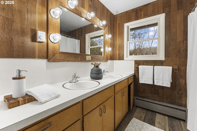 full bath featuring a sink, a baseboard radiator, wood walls, and double vanity