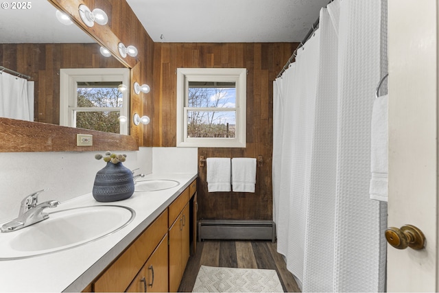 full bath with a sink, a baseboard heating unit, wooden walls, and double vanity