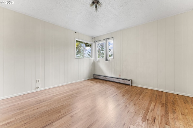 spare room featuring baseboards, baseboard heating, wood finished floors, and a textured ceiling