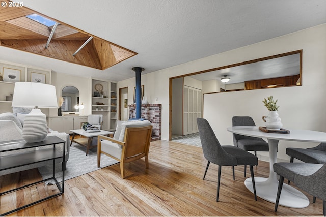 living area featuring light wood finished floors, built in features, a skylight, a wood stove, and a textured ceiling