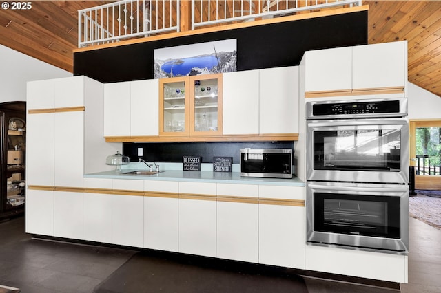 kitchen featuring stainless steel appliances, vaulted ceiling, a sink, light countertops, and glass insert cabinets