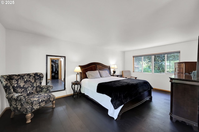 bedroom with a spacious closet, dark wood-style floors, and baseboards
