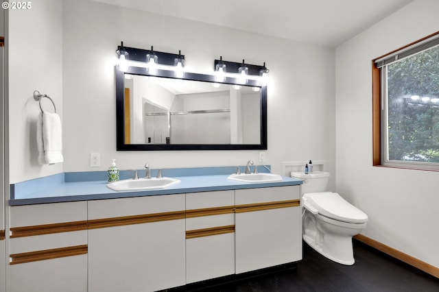 bathroom with a stall shower, toilet, wood finished floors, double vanity, and baseboards