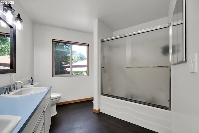 full bath with toilet, double vanity, enclosed tub / shower combo, baseboards, and wood finished floors