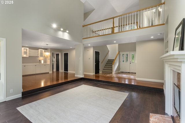 unfurnished living room with baseboards, stairs, a high ceiling, and hardwood / wood-style floors