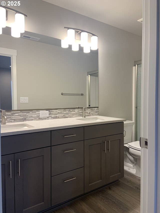 bathroom featuring visible vents, a sink, decorative backsplash, and wood finished floors
