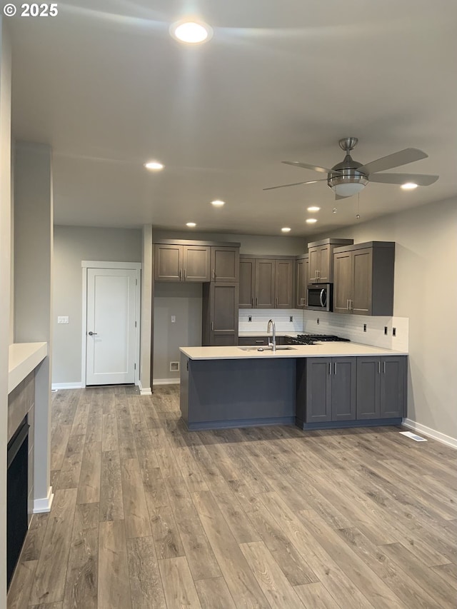 kitchen with a ceiling fan, light countertops, baseboards, stainless steel microwave, and light wood finished floors