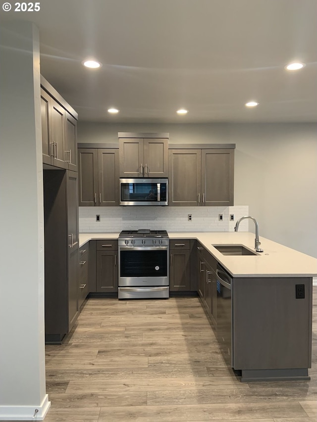 kitchen with appliances with stainless steel finishes, tasteful backsplash, a sink, a peninsula, and light wood-style floors