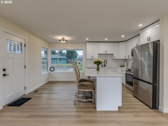 kitchen with white cabinets, a center island, stainless steel appliances, light hardwood / wood-style flooring, and a breakfast bar area