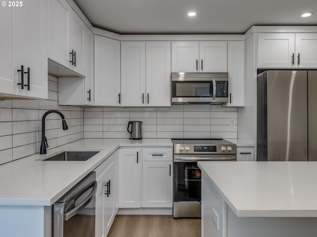 kitchen with white cabinets, light wood-type flooring, appliances with stainless steel finishes, and sink